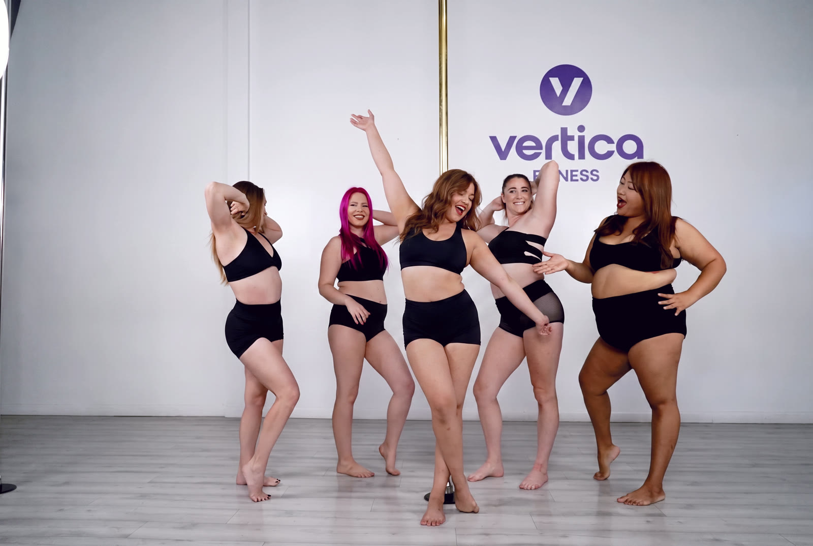Vertica members of all ages and body types laughing together in a pole fitness class